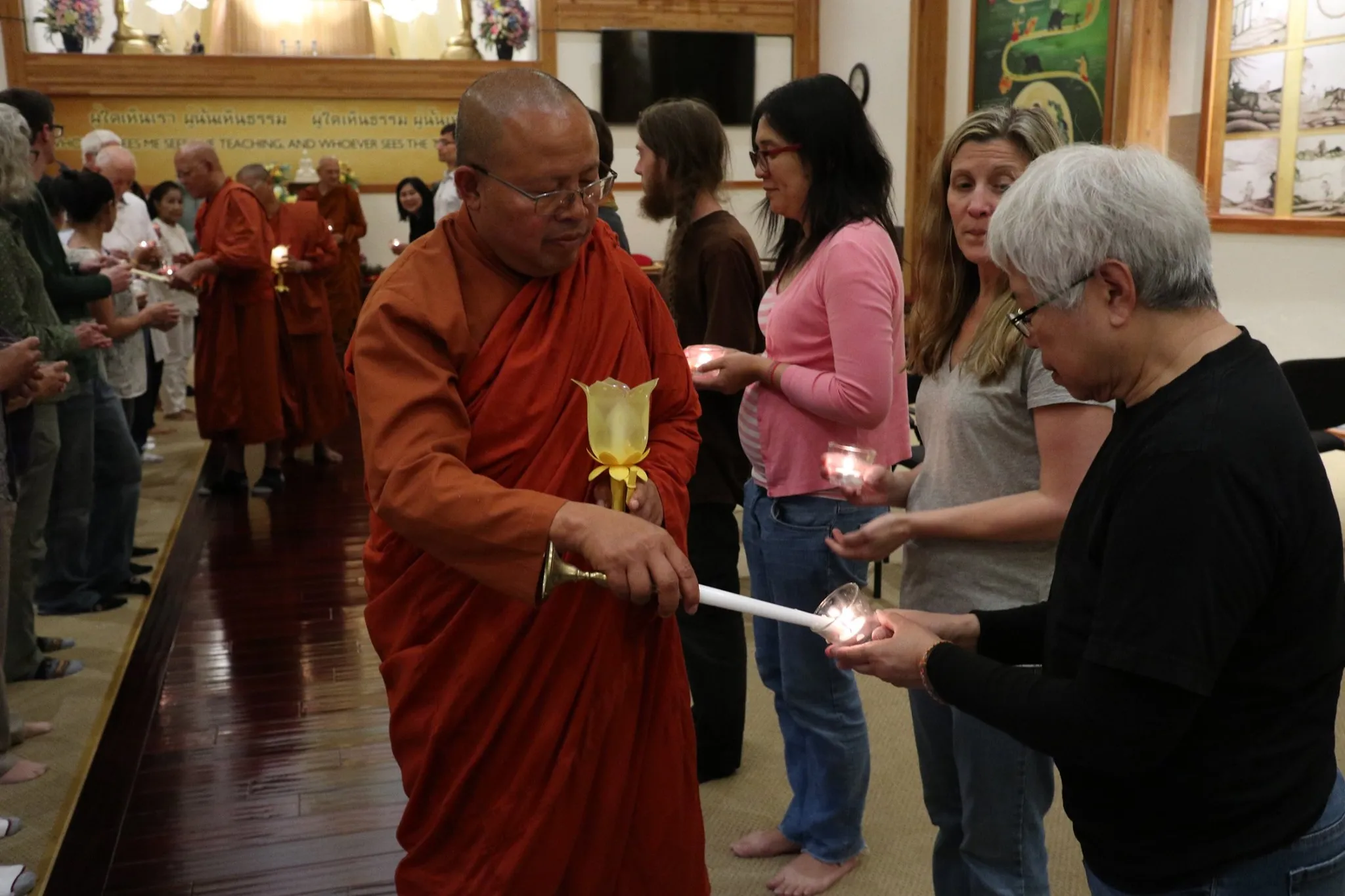 A monk lighting a candle for a woman at the Asalha Puja Day event